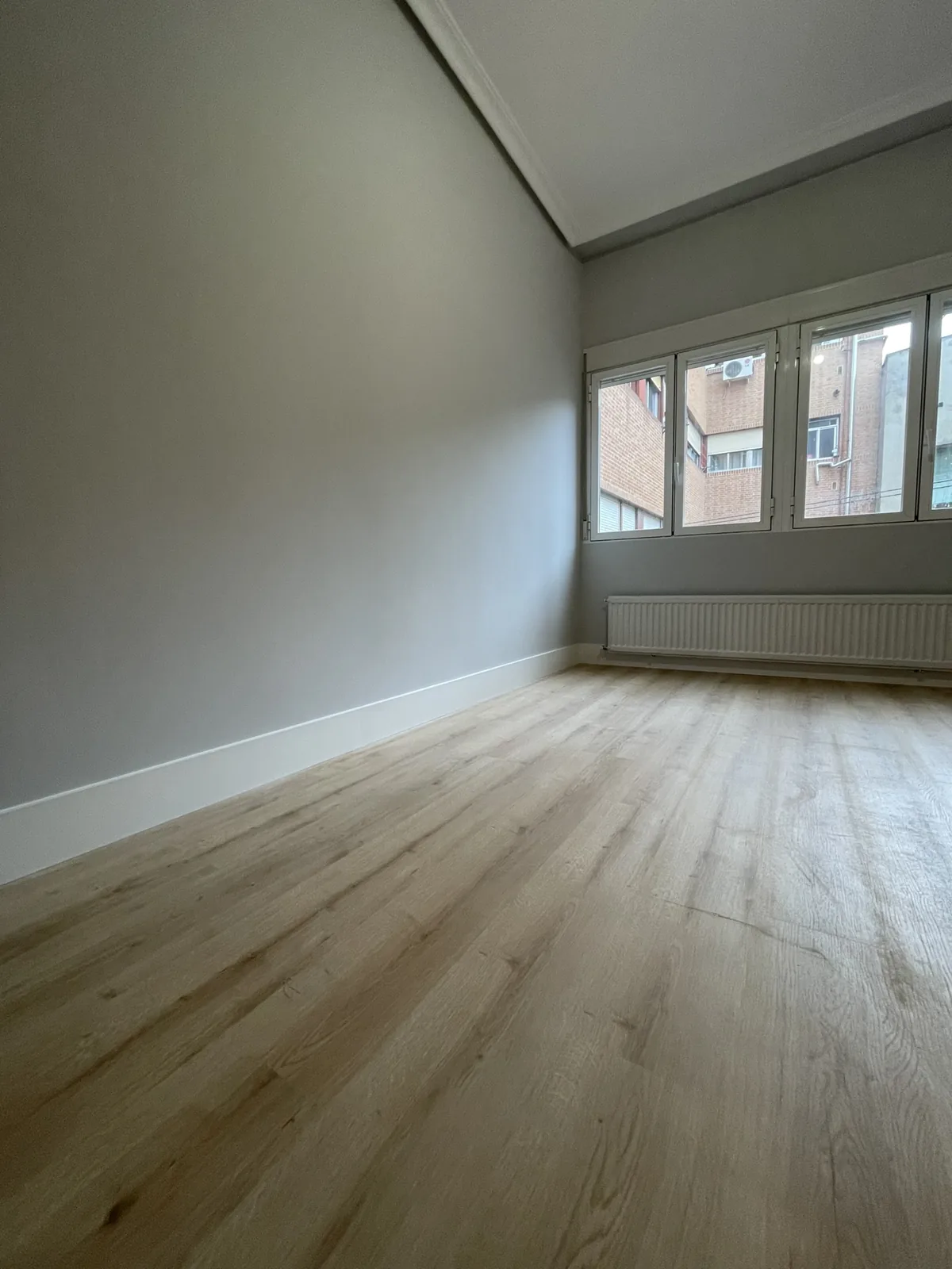 Habitación reformada con suelo laminado color roble y rodapié blanco de 15 cm